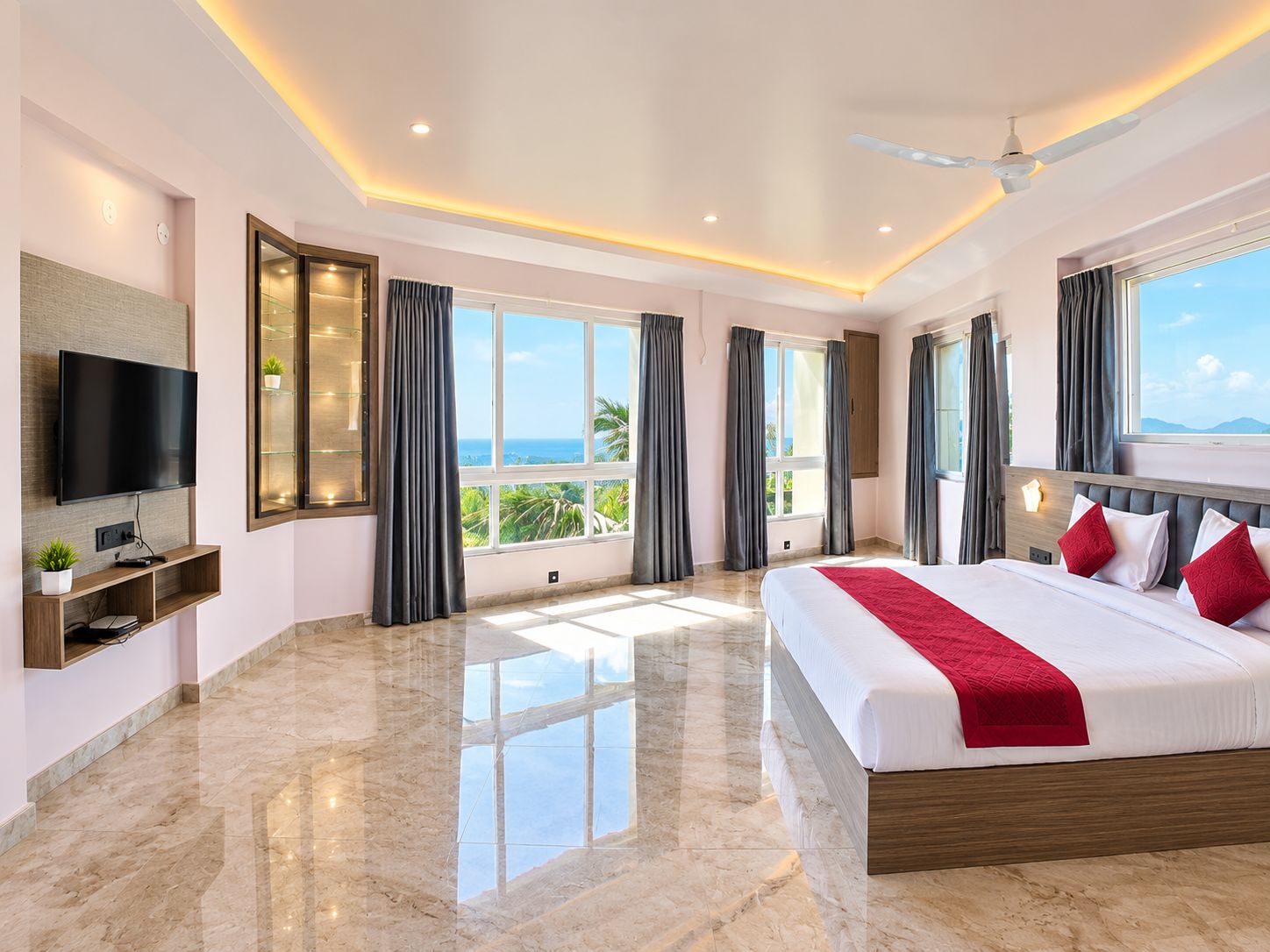 A modern hotel room with a large bed, a flat-screen TV, a balcony with a view, and a ceiling fan.