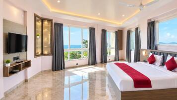 A modern hotel room with a large bed, a flat-screen TV, a balcony with a view, and a ceiling fan.