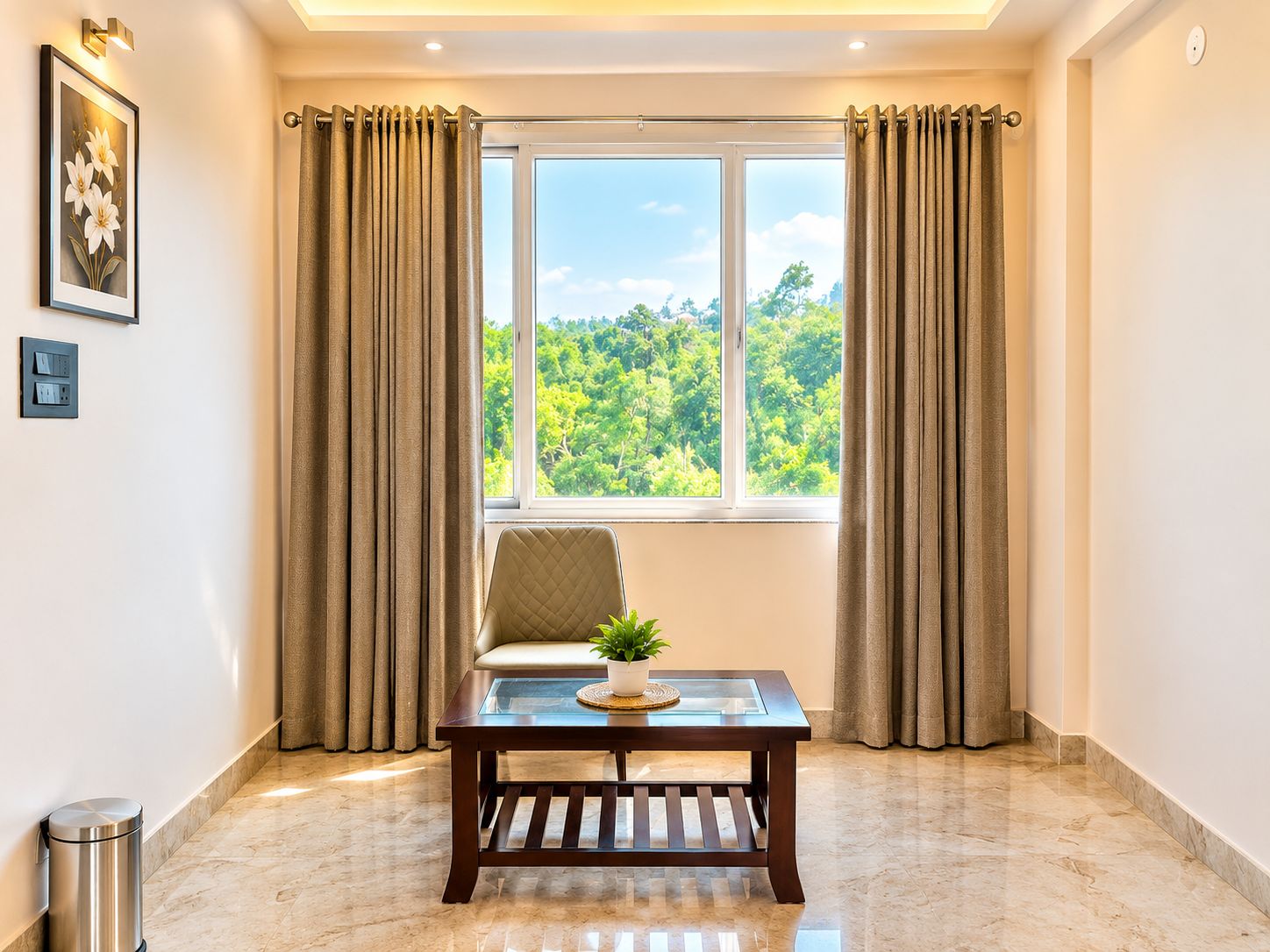 A room with a large window, a cushioned chair, a small table with a plant, and a trash bin.