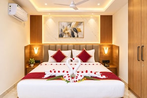 Habitación de hotel con una cama grande, dos mesitas de noche, aire acondicionado de pared, ventilador de techo y un armario de madera.