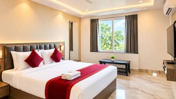 Habitación de hotel con una cama grande, ventilador de techo, equipo de aire acondicionado, televisor y ventana con cortinas.