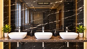 Een moderne badkamer met drie wasbakken, marmeren wanden en een bordje voor handenwassen.