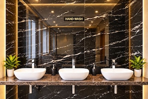 Un baño moderno con tres lavamanos, paredes de mármol y un letrero de lavado de manos.