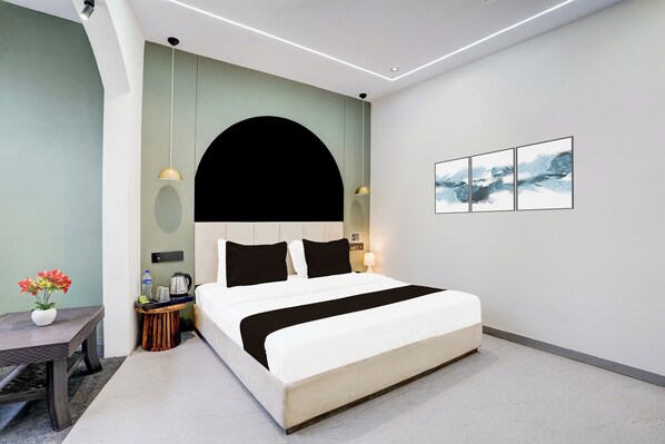 A modern hotel room with a bed, bedside tables, a small table with flowers, and a painting on the wall.