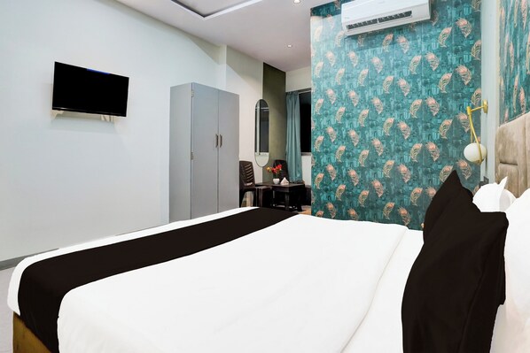 A hotel room with a bed, a flat-screen TV, a wardrobe, a desk with a chair, and a mirror. - Collection O Adajan Formerly Hotel Sky (Surat)