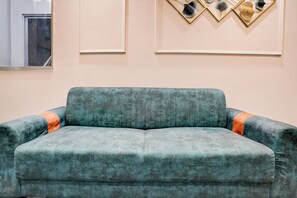 A teal sofa with orange accents in a room with a light-colored wall and decorative wall art. - Collection O Adajan Formerly Hotel Sky (Surat)