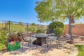 Un patio al aire libre con una mesa y sillas, rodeado de plantas en macetas y una valla metálica.