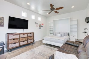 Ein modernes Schlafzimmer mit Bett, einer Couch, einem Fernseher und einem Deckenventilator.