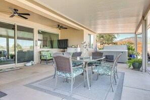 Ein überdachter Patio-Bereich mit Esstisch und Stühlen, einem Deckenventilator und Blick auf die umliegende Landschaft.