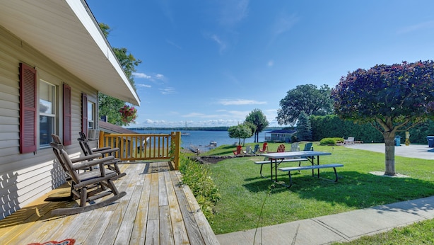 A wooden deck with outdoor furniture, a grassy lawn, and a view of the water. - Private Beach Access! Lake Champlain Cabin (Plattsburgh)