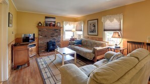 A cozy living room with a fireplace, a sofa, a television, and a table. - Private Beach Access! Lake Champlain Cabin (Plattsburgh)