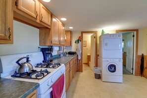 A kitchen with wooden cabinets, a gas stove, a coffee maker, and a stacked washer-dryer unit. - Fire Pit & Views! Lake Champlain Shoreline Stay (Plattsburgh)