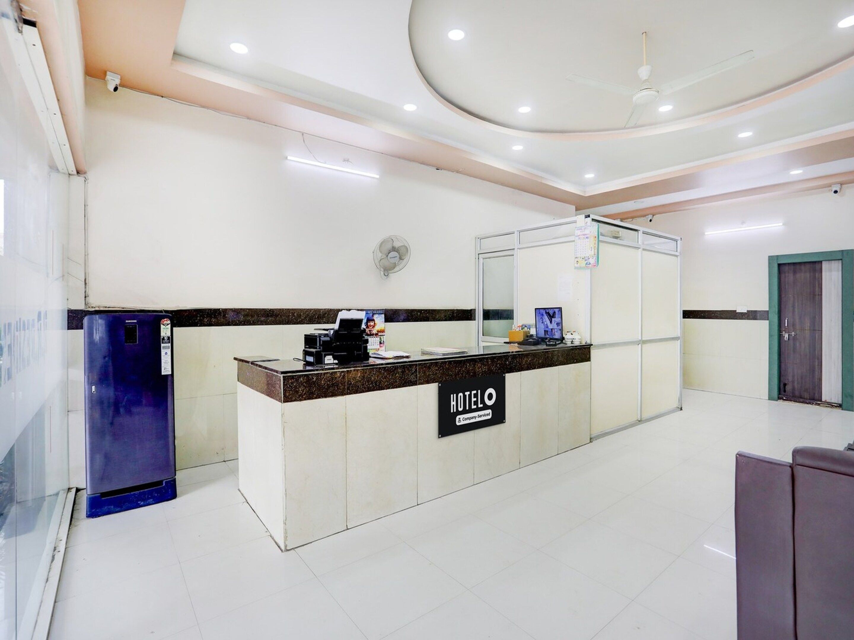 Zona de recepción de un hotel, con un mostrador, una computadora y un ventilador de pared.