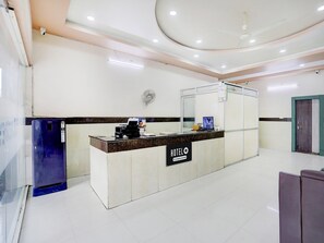 A hotel reception area with a reception desk, a computer, and a wall-mounted fan.