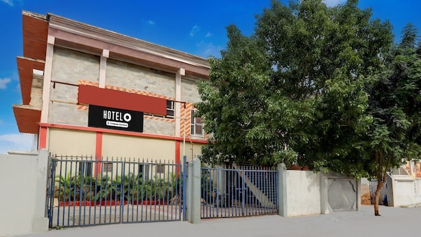 A hotel with a signboard, a gated entrance, and a large tree in front.