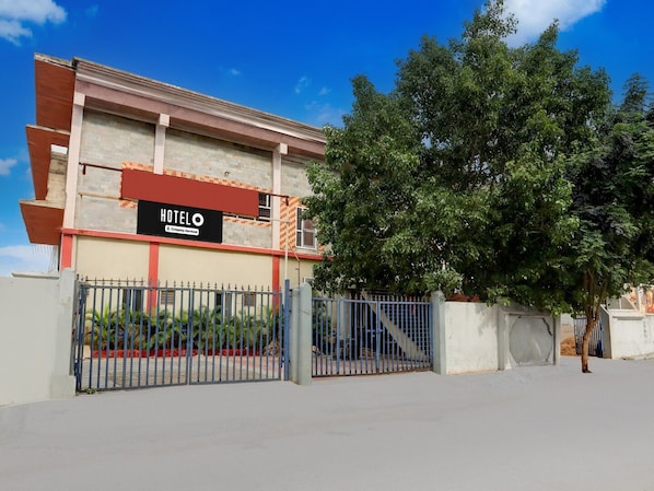 A hotel with a signboard, a gated entrance, and a large tree in front.