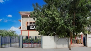 A hotel with a signboard, a gated entrance, and a tree in the foreground.
