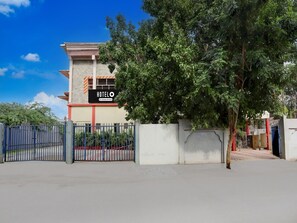 A hotel with a signboard, a gated entrance, and a tree in the foreground.