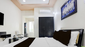 A hotel room with a bed, a desk, a chair, a telephone, and a wall-mounted TV.