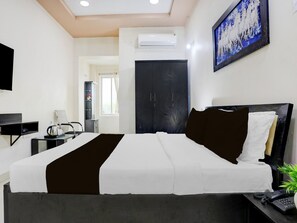 A hotel room with a bed, a desk, a chair, a telephone, and a wall-mounted TV.