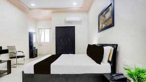 A modern hotel room with a bed, a desk, a chair, a wardrobe, and a potted plant.