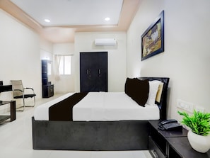A modern hotel room with a bed, a desk, a chair, a wardrobe, and a potted plant.
