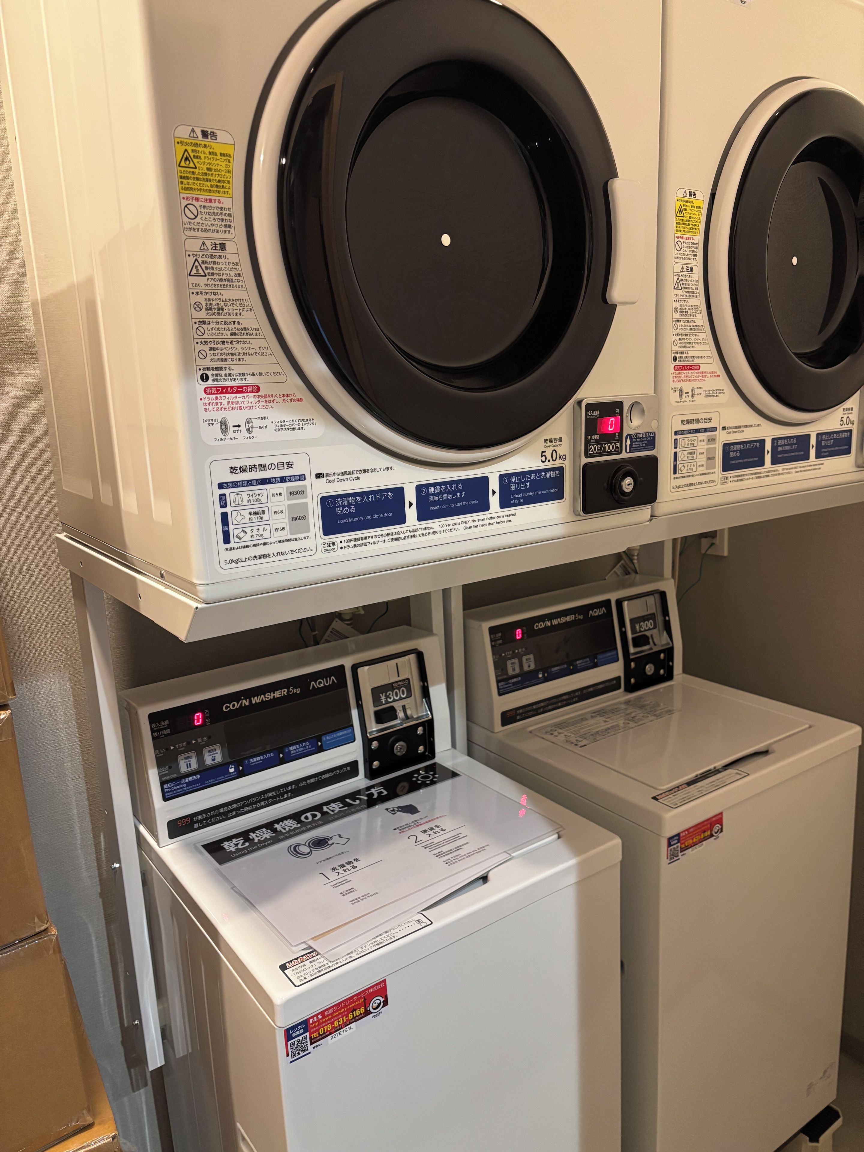 A laundry facility with multiple washing machines and dryers, control panels, and safety instructions.