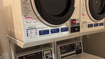 A laundry facility with multiple washing machines and dryers, control panels, and safety instructions.