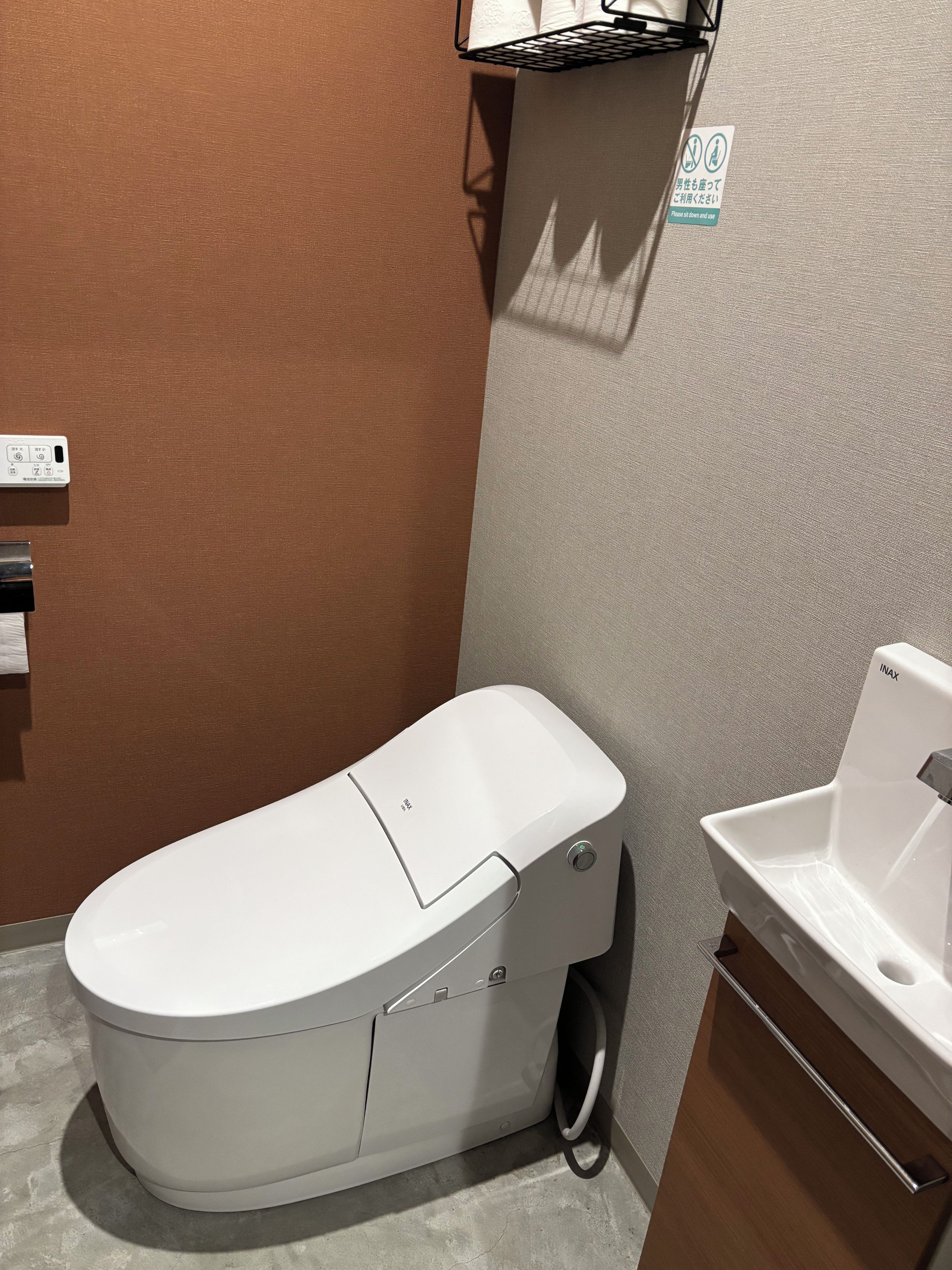 Un baño moderno con inodoro blanco, lavamanos empotrado y un perchero.