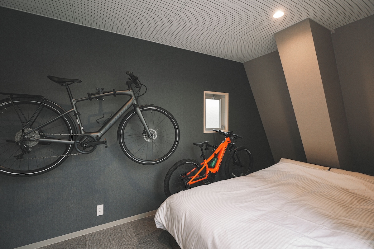 A bedroom with a bed, two bicycles, a window, and a ceiling with a grid pattern.