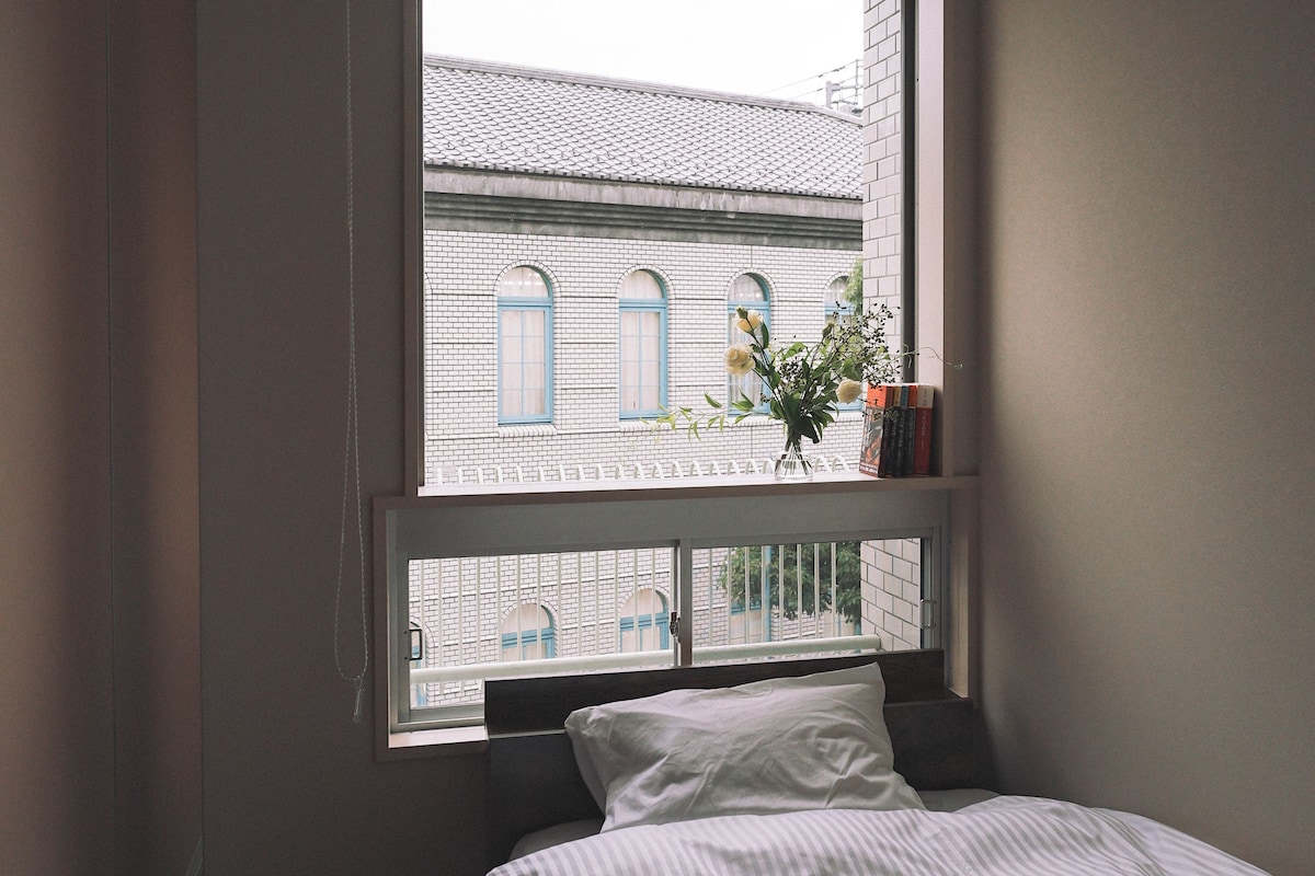 A bedroom with a bed, a window, and a view of a building with blue windows.