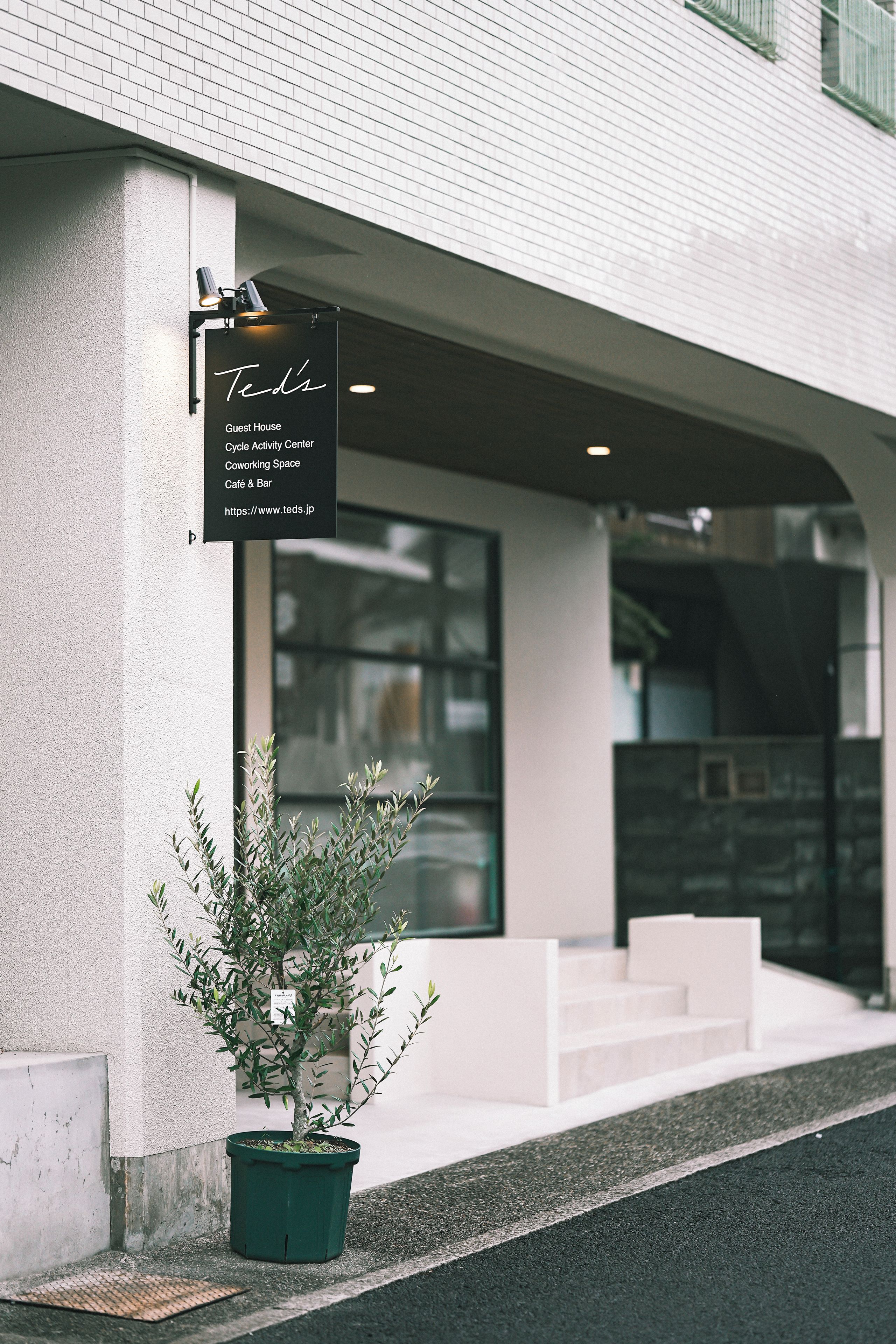 A building with a sign indicating it is a guest house, cycle activity center, coworking space, café & bar, and includes a URL.