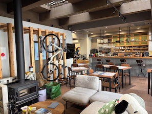 A cozy interior with a wood-burning stove, seating area, and a bar with kitchen in the background. - Ted's guesthouse (Uchiko)