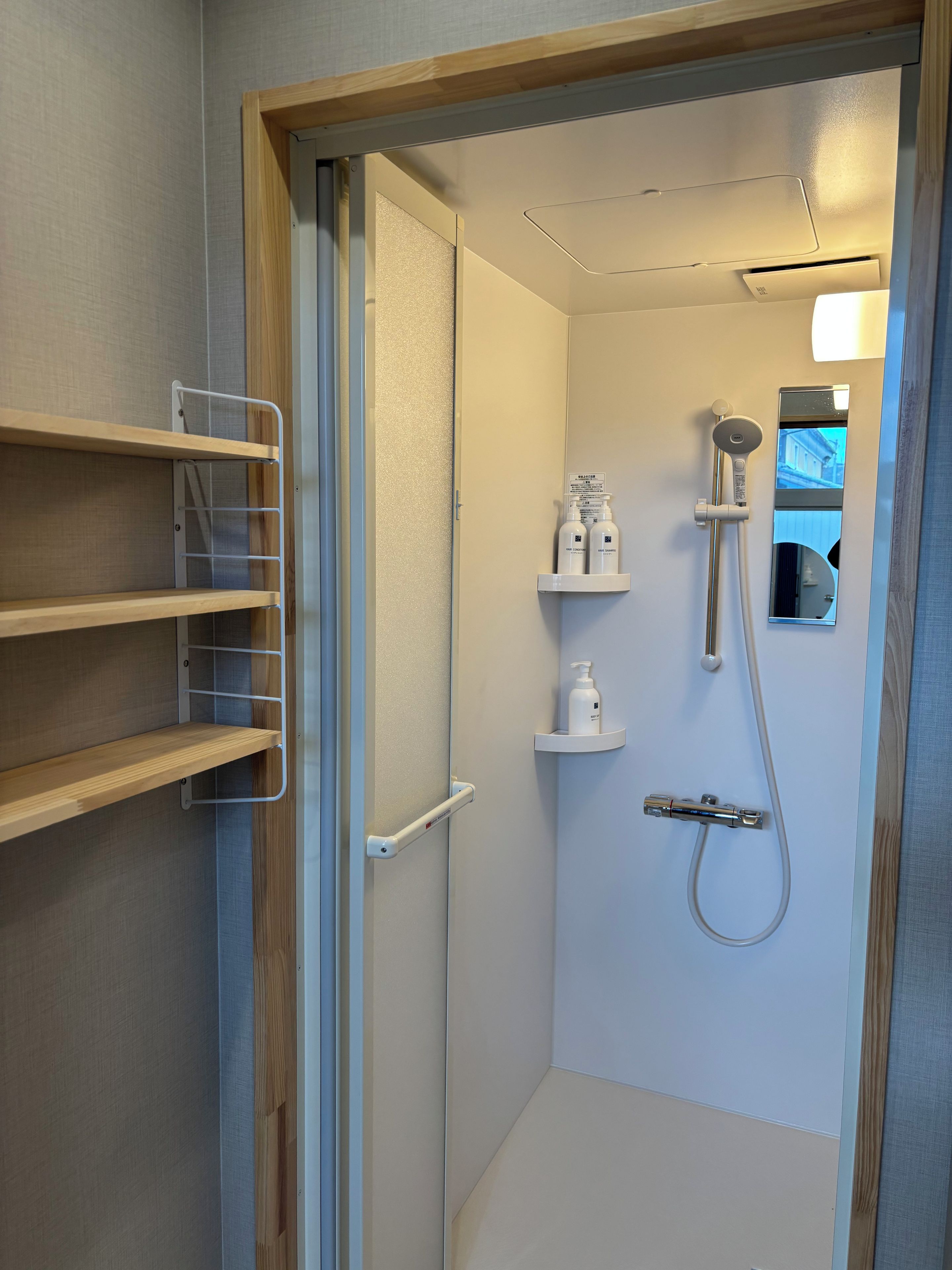 A bathroom with a shower, a mirror, and a shelf with toiletries.