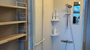 A bathroom with a shower, a mirror, and a shelf with toiletries.