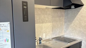 A modern kitchen with a built-in refrigerator, a stainless steel sink, and a black range hood. - Ted's guesthouse (Uchiko)