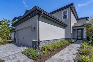 A two-story residential building with a garage, stone foundation, and landscaped garden with various plants and a pathway. - 10 Mi to Disney & Old Town! Stylish Family Home (Kissimmee)