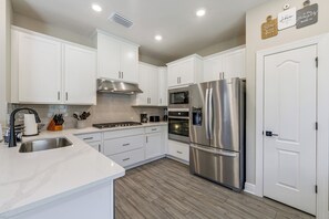 A modern kitchen with white cabinets, stainless steel appliances, and a wooden floor. - 10 Mi to Disney & Old Town! Stylish Family Home (Kissimmee)