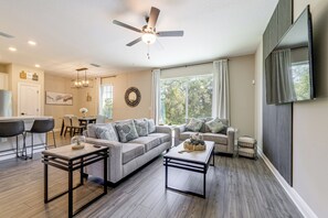 A modern living room with a sofa, coffee table, and a dining area with chairs. - 10 Mi to Disney & Old Town! Stylish Family Home (Kissimmee)