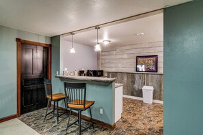 A kitchen with a bar area, two chairs, a trash can, and a framed picture on the wall.