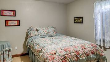 A bedroom with a floral bedspread, a small round table, and two framed items on the wall.