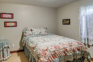 A bedroom with a floral bedspread, a small round table, and two framed items on the wall.