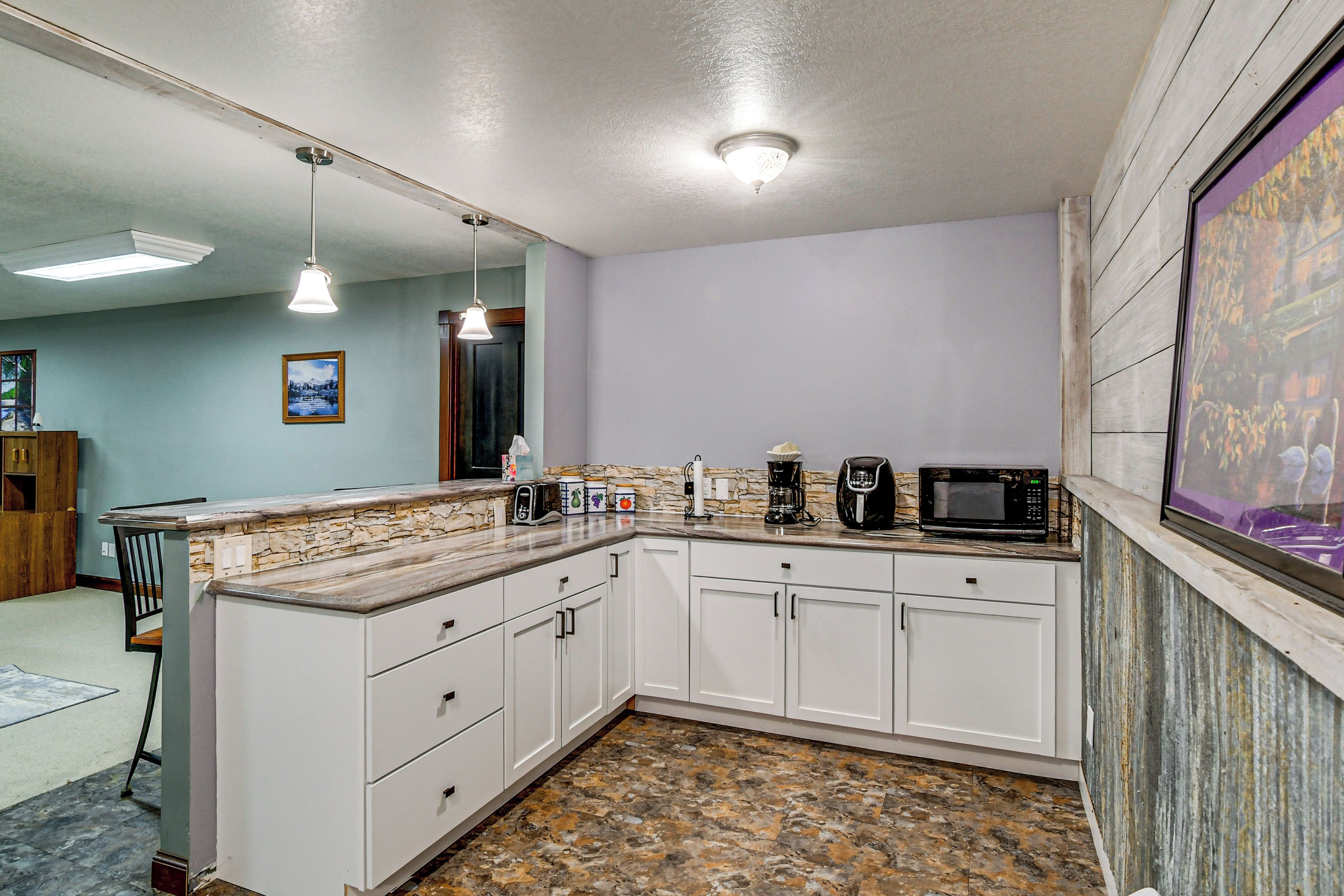 A kitchen with white cabinets, a granite countertop, a coffee maker, a microwave, and pendant lighting.