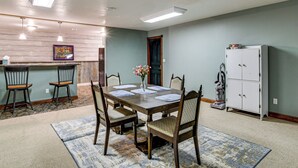 Ein Essbereich mit einem Holztisch, gedeckt für vier Personen, umgeben von Stühlen, einer Blumenvase und einer Küche mit Schränken und einem Kühlschrank.