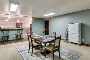 Ein Essbereich mit einem Holztisch, gedeckt für vier Personen, umgeben von Stühlen, einer Blumenvase und einer Küche mit Schränken und einem Kühlschrank.