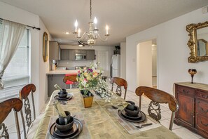 Ein Esszimmer mit einer Chandelüster, einem Tisch für vier Personen und einer Küche im Hintergrund.