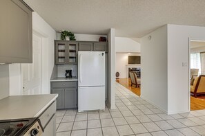 Una cocina con armarios grises, un refrigerador blanco y una zona de comedor con mesa y sillas de madera.