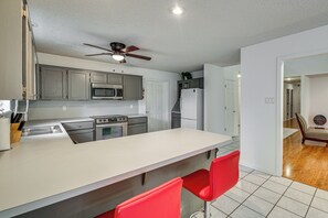 Una cocina moderna con gabinetes grises, electrodomésticos de acero inoxidable, una encimera blanca y un ventilador de techo.