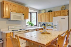 A kitchen with wooden cabinets, a microwave, a stove, a refrigerator, and a dining table with chairs.