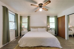 Un dormitorio con una cama, dos mesitas de noche, un ventilador de techo y una ventana con cortinas.